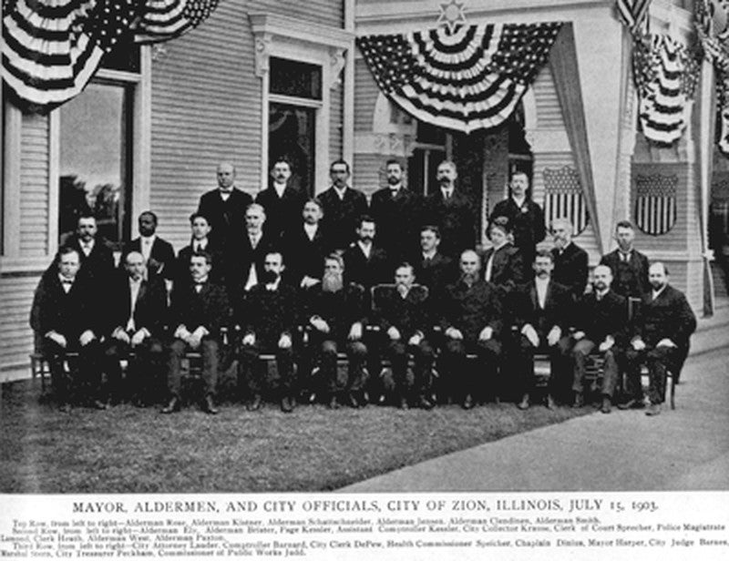 Men sitting for portrait in front of building festooned with American flags